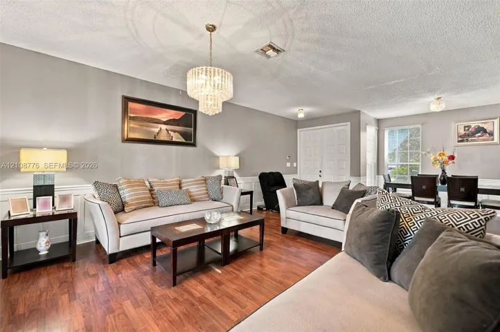 Living area featuring wood-finish flooring, wainscoting, tiered crystal chandelier, double-door entrance, and multi-pane window