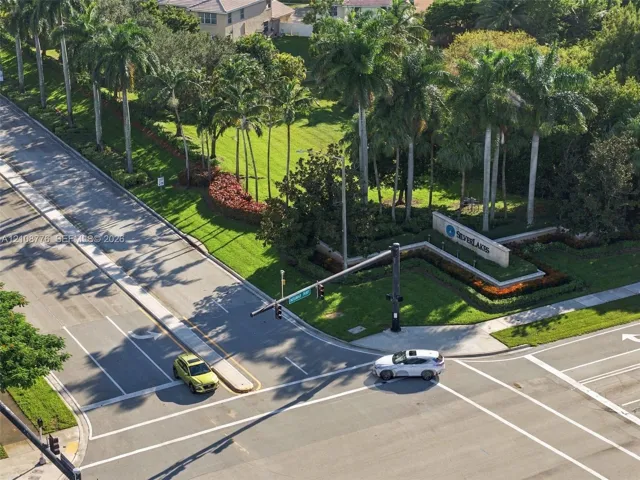 Community entrance featuring mature palm trees, landscaped green space, and prominent stone-finish signage