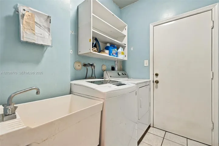 Utility space featuring a basin sink with a chrome faucet, built-in shelving, tiled flooring, and a dedicated exterior access door