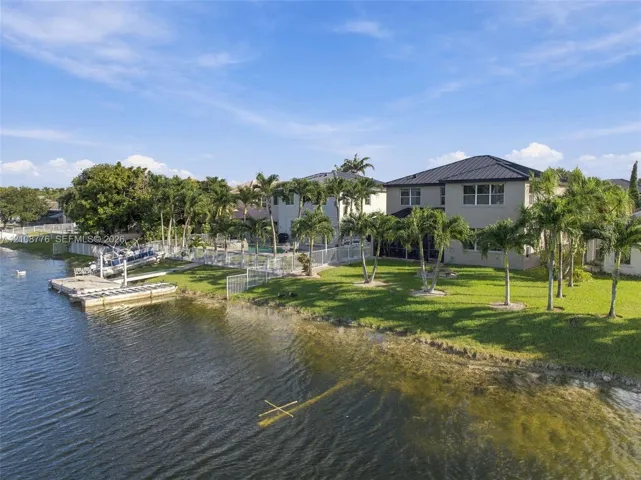 Waterfront exterior featuring a private boat dock, metal roofing, expansive lawn, and mature palm trees