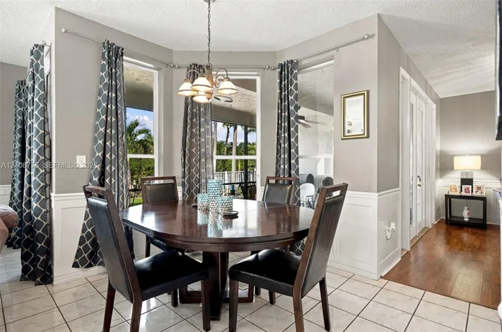 Dining area featuring a bay window, tile flooring, wainscoting, and a multi-light chandelier