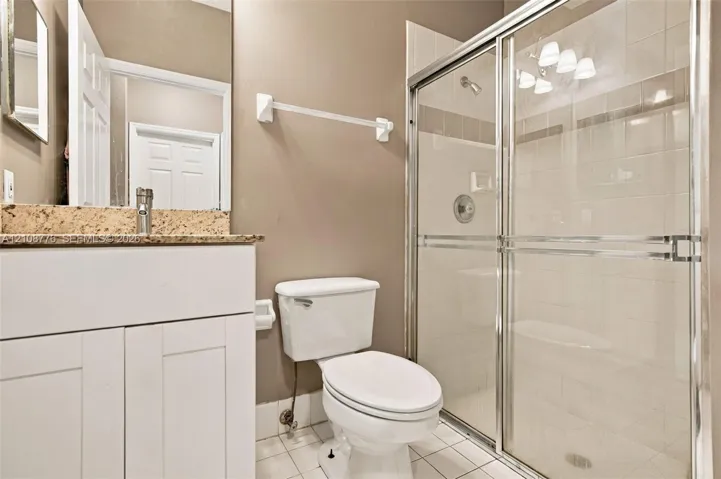 Bathroom featuring a white vanity cabinet with a speckled stone countertop, a glass-enclosed shower with tiled surround, and ceramic tile flooring