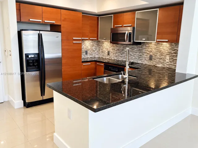 Kitchen featuring flat-panel wood cabinetry, dark stone countertops, stainless steel appliances, multi-tonal mosaic tile backsplash, and a gooseneck faucet