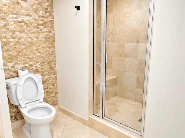 Shower featuring large-format tile surround, integrated bench seating, and a glass door enclosure, complemented by a textured stone accent wall and neutral tile flooring