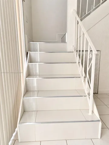 Staircase featuring glossy tile steps, metallic trim edges, and a white decorative metal railing