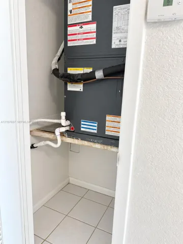 Utility closet featuring an installed HVAC air handler unit, mounted thermostat, and tiled flooring