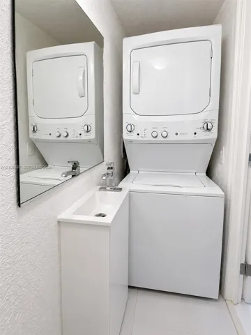 Stacked laundry unit, wall-mounted mirror, white pedestal-style sink, and chrome single-handle faucet