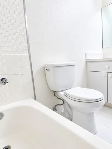 Bathroom featuring a white porcelain tub with integrated tile surround, ceramic wall accent tiling, and vanity cabinetry with a solid-surface countertop