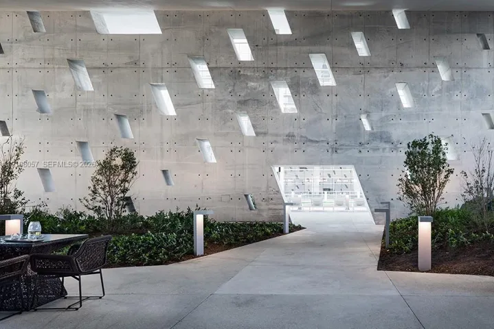 Architectural concrete wall featuring a geometric pattern of recessed window openings, cast-in-place construction, integrated landscape lighting, and concrete paved hardscaping