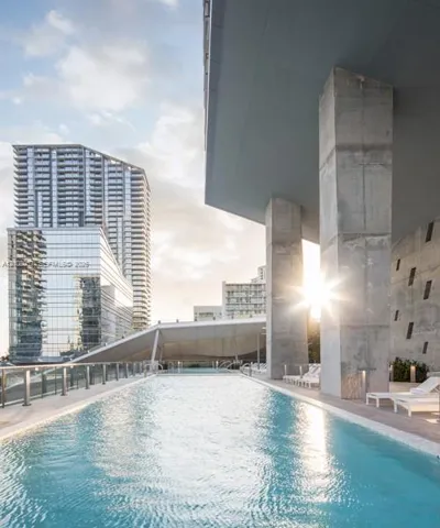 Outdoor swimming pool featuring a concrete deck, glass panel railings, and structural concrete columns