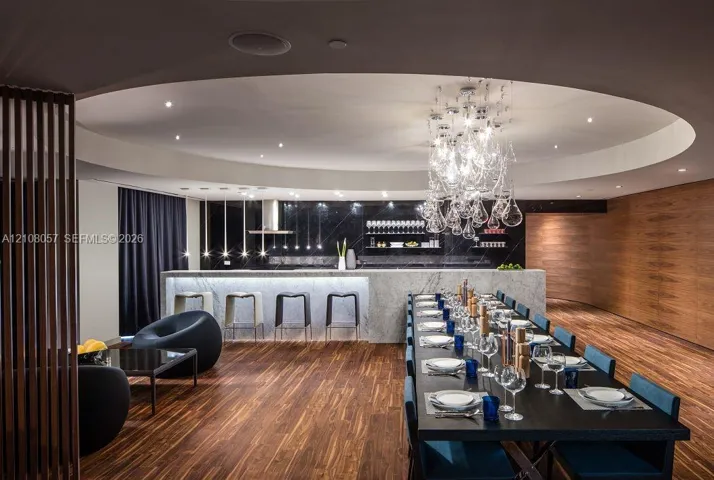 Circular recessed ceiling detail with a sculptural glass chandelier, wood-finish flooring, full-height wood-paneled walls, and a stone-topped island with integrated under-cabinet lighting