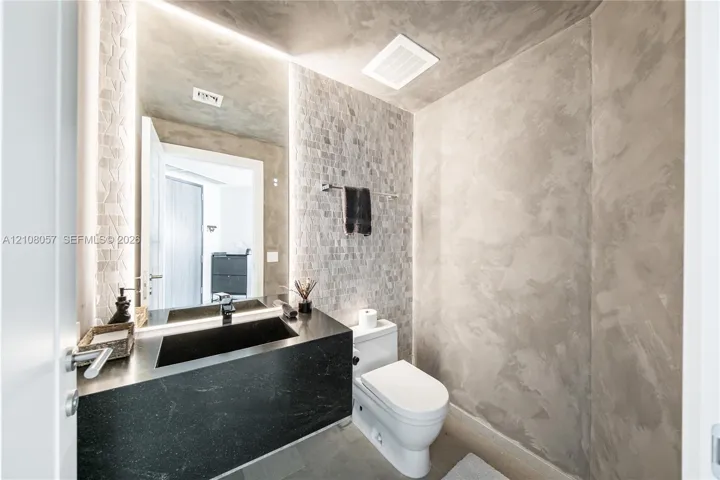 Bathroom featuring textured wall finishes, a floating black countertop with an integrated basin, vertical recessed LED lighting, and mosaic-tiled accent wall