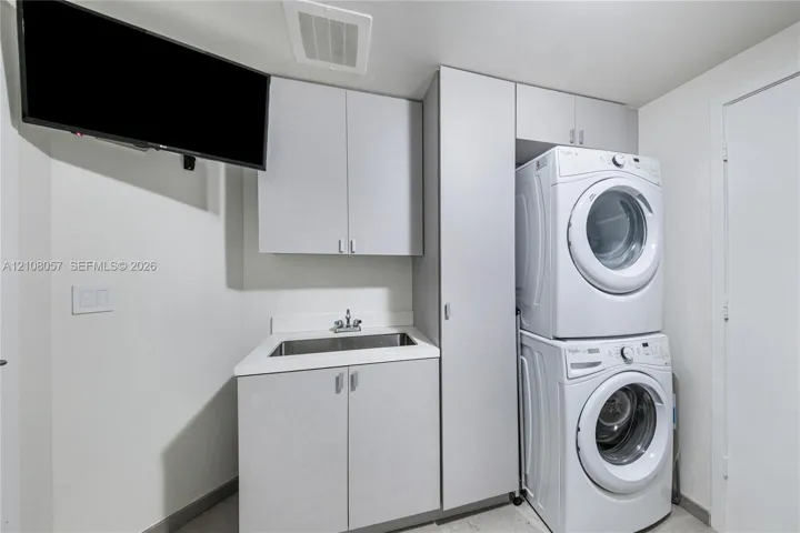 Laundry room featuring cabinetry with light-colored laminate finishes, a rectangular drop-in sink, and a vertical stacked laundry center