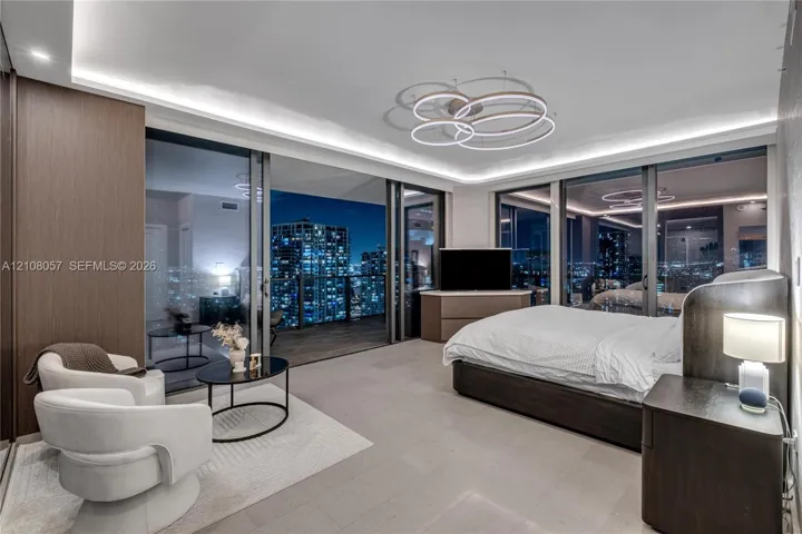 Floor-to-ceiling glass sliding doors, recessed cove lighting, sculptural multi-ring chandelier, large-format tile flooring, and integrated wood-veneer wall paneling