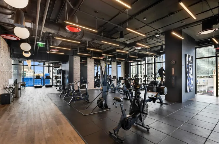 Fitness center featuring industrial-style exposed ceilings, wood-finish flooring, rubber matting, floor-to-ceiling windows, and linear LED lighting