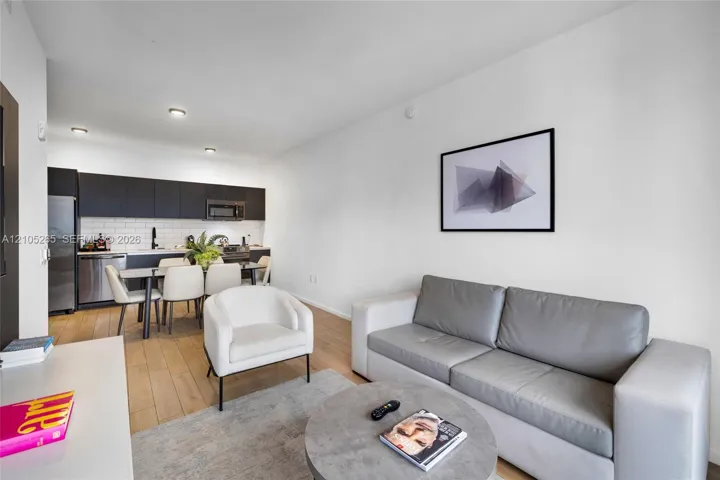 Modern kitchen featuring matte black flat-panel cabinetry, white subway tile backsplash, stainless steel appliances, and wood-finish flooring