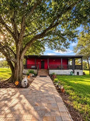 Exterior featuring a metal-sided structure with a covered front porch, concrete foundation, and a wide paver stone walkway beneath a large mature tree