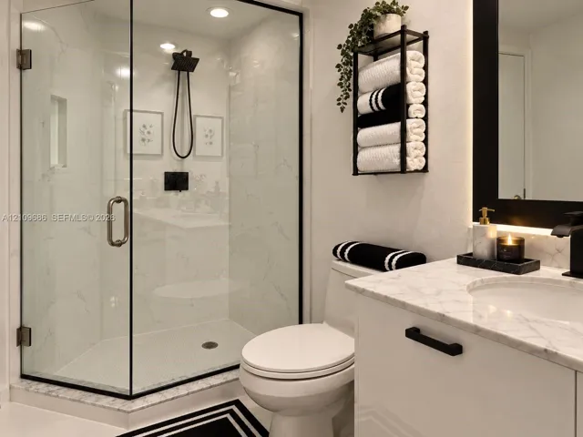 Walk-in shower with black-trimmed glass enclosure, stone-finish wall tile, and black rainfall showerhead