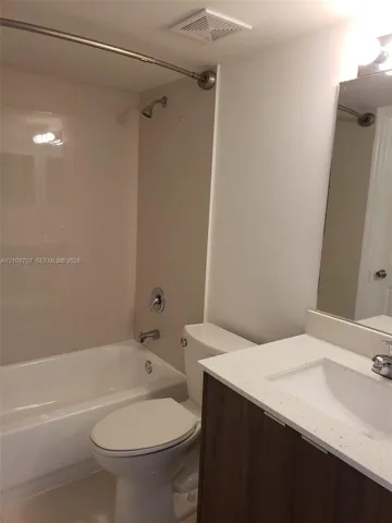 Bathroom featuring a wood-finish vanity with a light-toned countertop, integrated basin, tub-shower combination with light-toned wall surrounds, and a wall-mounted mirror