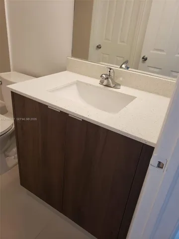 Vanity featuring dark wood-finish cabinetry, a white countertop, an integrated rectangular sink, a chrome faucet, and an expansive wall-mounted mirror