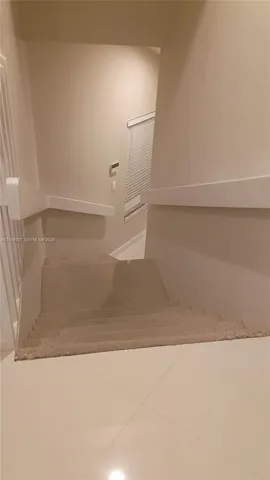 Staircase featuring wall-mounted railings, carpeted treads, and tiled flooring at the landing