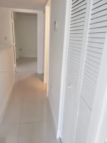 Hallway featuring polished tile flooring and white louvered closet doors