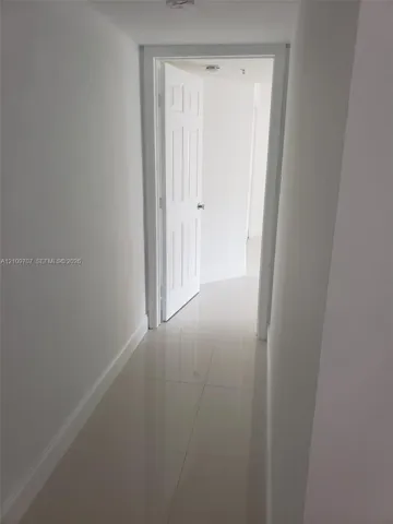Hallway featuring large-format ceramic tile flooring and a six-panel interior door with brushed metal hardware