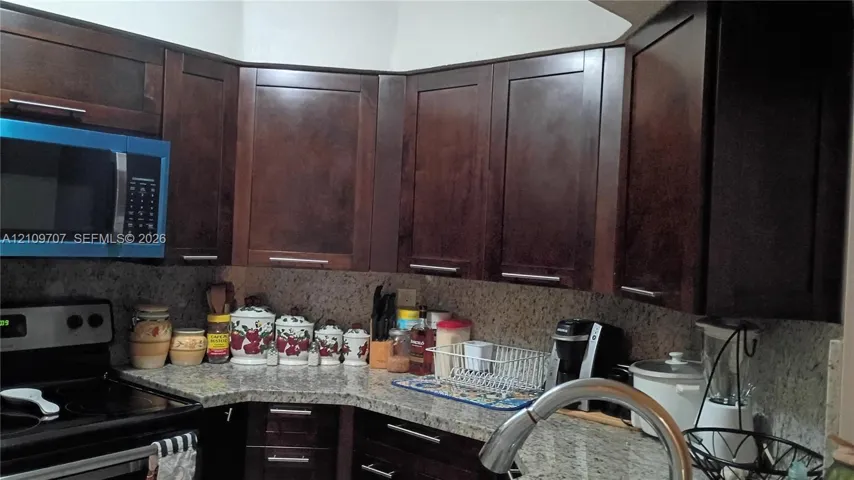 Dark-finish cabinetry with modern hardware, stone-composite countertops, and a stainless steel pull-down kitchen faucet