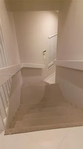 Staircase featuring neutral carpeting, white vertical balusters, and a solid wall-mounted handrail