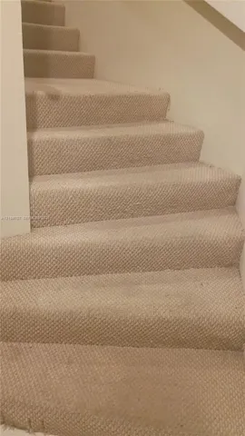 Staircase featuring neutral-toned textured wall-to-wall carpeting and plain drywall finish