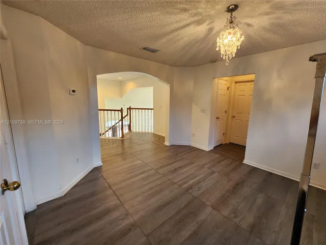 Wood-finish flooring, ornate crystal chandelier, arched entryway, and wooden staircase railing