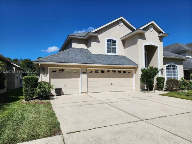 Two-story stucco exterior featuring a gabled roofline, arched window detailing, and a three-car garage with decorative transom windows