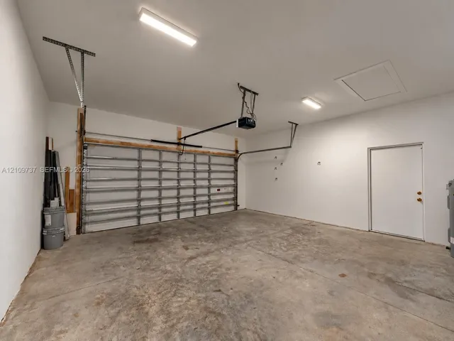 Multi-car garage featuring a motorized sectional door, concrete flooring, dual overhead LED lighting fixtures, and a separate side entry door