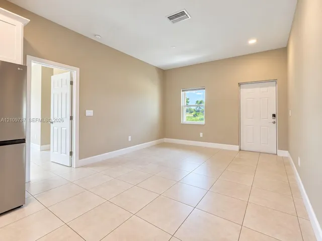 Neutral-toned room featuring large-format ceramic tile flooring, recessed lighting, and a solid-core exterior entry door