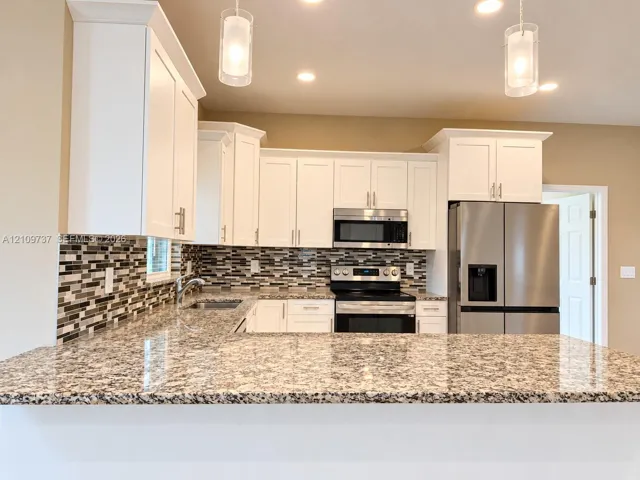Kitchen featuring white cabinetry, stone-patterned countertops, a multi-tone tile backsplash, stainless steel appliances, and pendant lighting