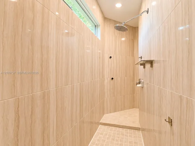 Walk-in shower featuring floor-to-ceiling stone-finish wall tile, a recessed transom window, a rainfall showerhead, a built-in stone shelf, and a mosaic tile shower floor