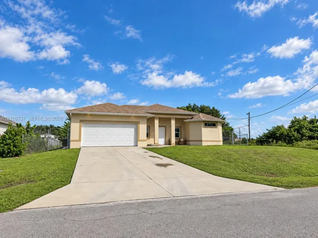 Single-story stucco exterior featuring a hip roof, two-car garage, concrete driveway, and expansive lawn