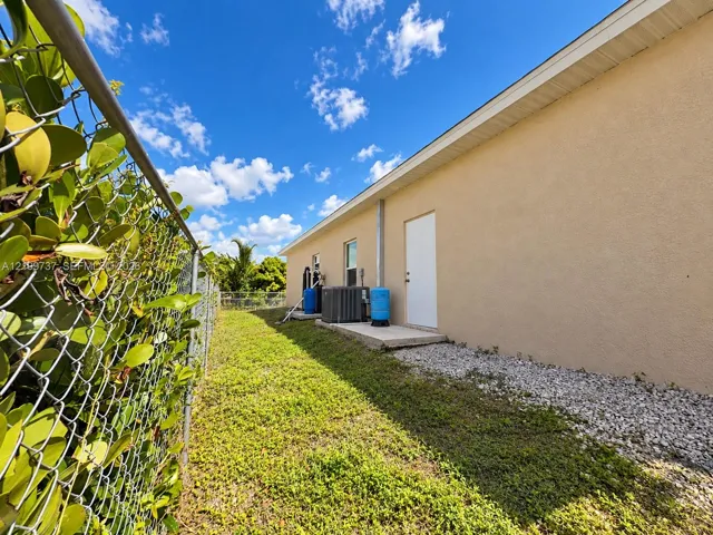 Exterior side yard featuring stucco siding, gravel ground cover, a chain-link fence, and installed utility equipment