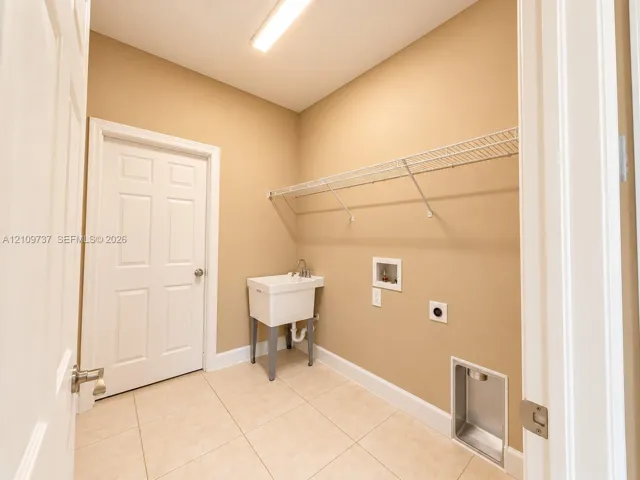 Utility area featuring ceramic tile flooring, a wall-mounted wire shelving system, a freestanding utility basin, and built-in laundry connections