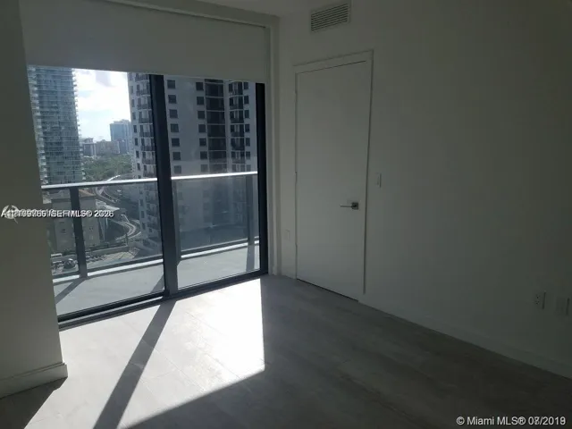 Floor-to-ceiling glass wall, private balcony with metal railing, and neutral tile flooring throughout