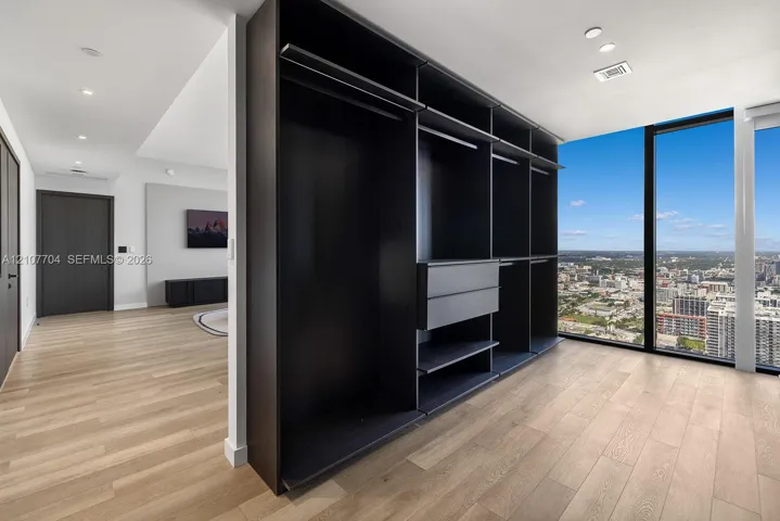 Custom-built dark finish storage cabinetry featuring integrated drawers and hanging rods, light-toned wood-finish flooring, and floor-to-ceiling windows