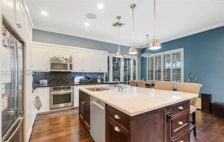Kitchen featuring white cabinetry, center island with dark wood-finish base and light countertop, stainless steel appliances, mosaic tile backsplash, and wood-finish flooring