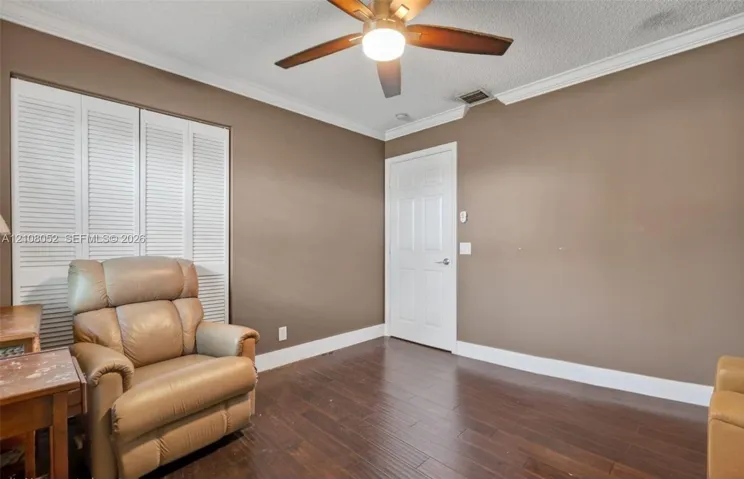 Wood-finish flooring, multi-panel interior door, louvered closet doors, ceiling fan with integrated lighting, and crown molding