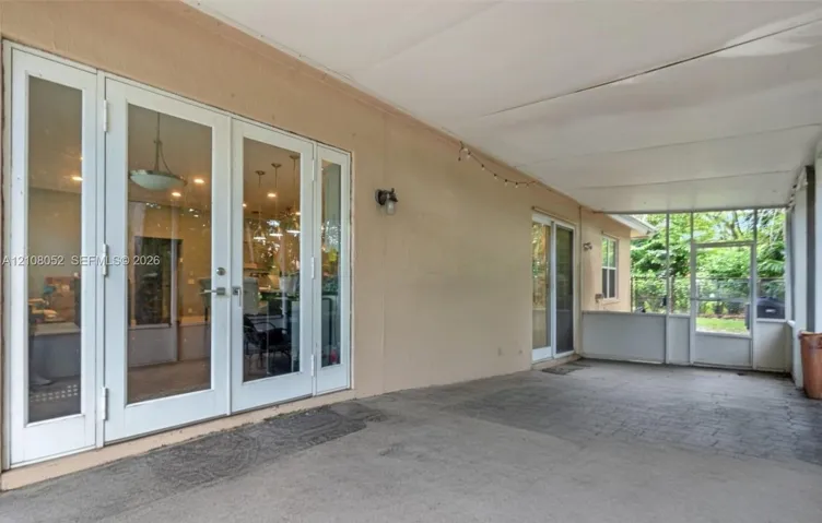 Covered patio featuring a paver-style flooring, double glass-paneled doors with side lights, and an integrated screened enclosure