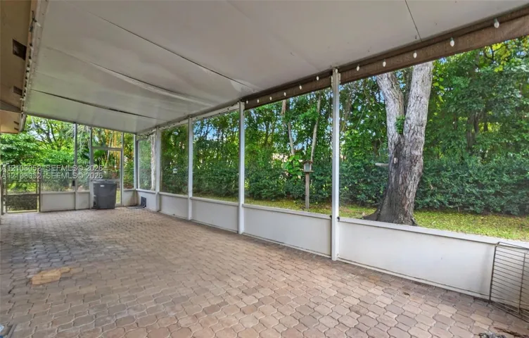 Screened-in patio featuring paver flooring, a white metal frame, and a solid roof covering