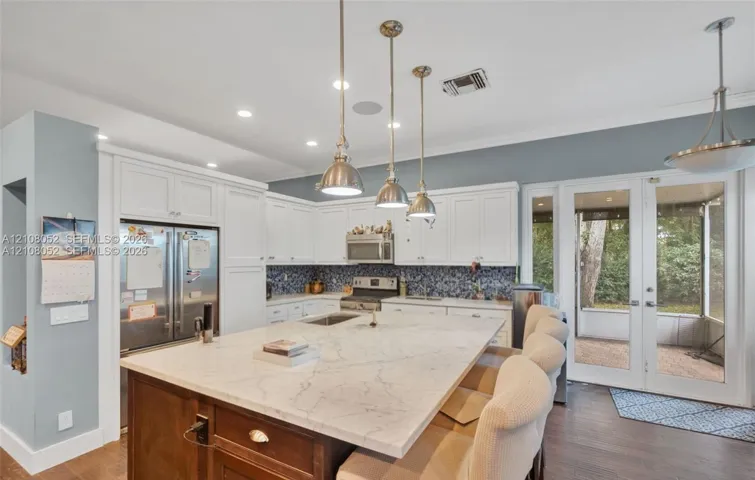 Kitchen featuring a large central island with a stone countertop, white shaker-style cabinetry, mosaic tile backsplash, recessed lighting, and metal pendant fixtures