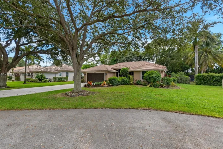 Single-story residence featuring a tiled roof, stucco exterior, attached garage, concrete driveway, and mature landscaping