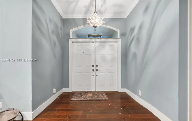 Entryway featuring double doors with a semi-circular transom window, wood-finish flooring, crown molding, and a tiered crystal chandelier