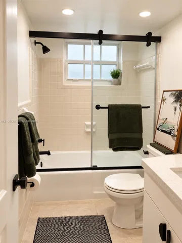Bathroom featuring a shower-tub combination, sliding glass door with matte black hardware, tile wall surround, and vanity with a light-toned countertop
