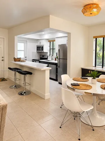 Kitchen featuring a quartz breakfast bar, stainless steel appliances, white cabinetry, tile flooring, and a flush-mount drum light fixture